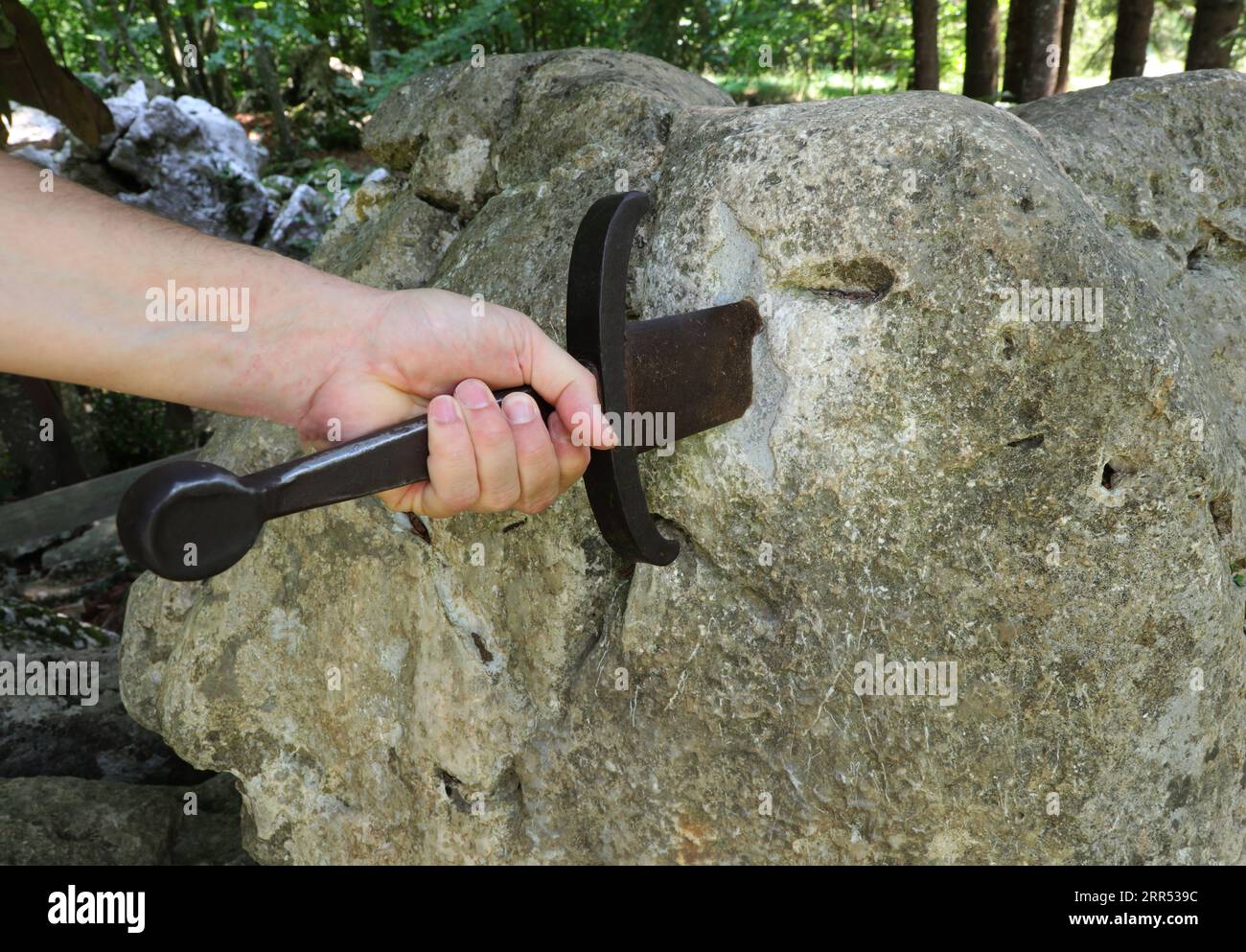 hand of the knight trying to extract the magic sword from the Rock in the middle of the forest Stock Photo