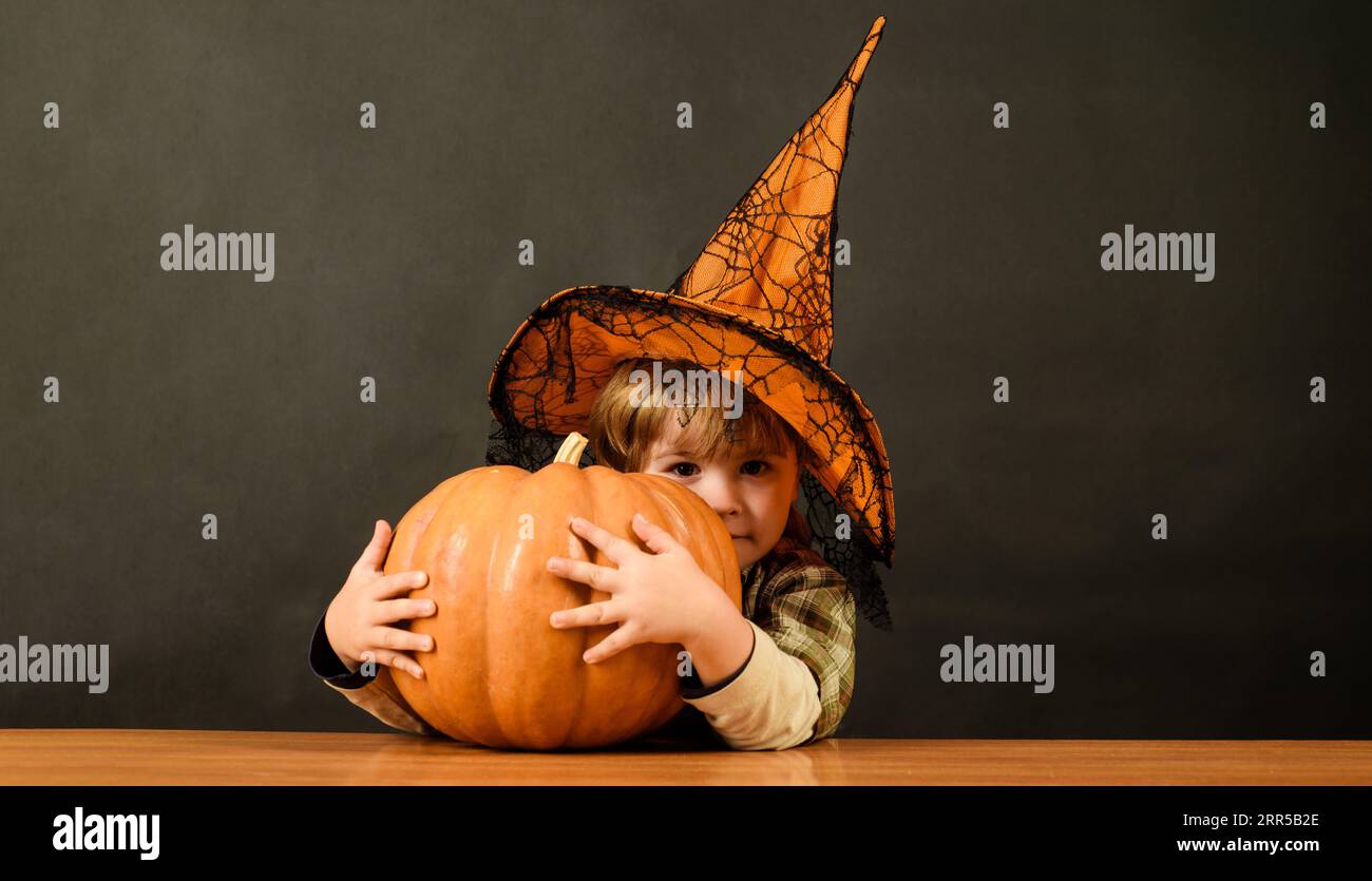 Little boy in witch hat with pumpkin. Halloween holidays. Cute child with pumpkin to Halloween. Autumn recipes. Thanksgiving day cooking or Halloween Stock Photo