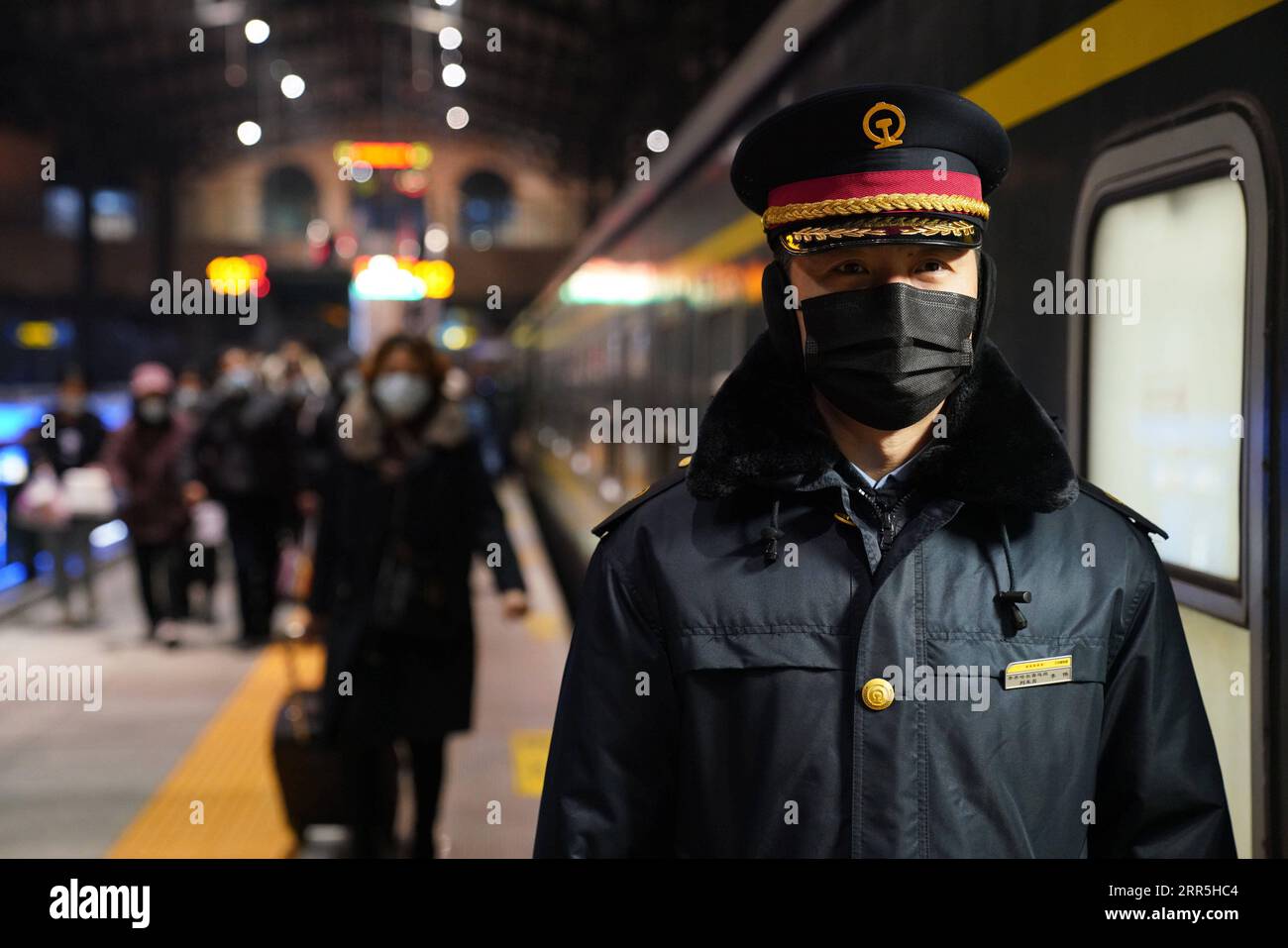 210107 -- HARBIN, Jan. 7, 2021 -- A staff member guides passengers outside train K7093 heading for Hailar, north China s Inner Mongolia Autonomous Region, at Harbin Railway Station in Harbin, northeast China s Heilongjiang Province, Jan. 6, 2021. Train No. K7093/4, connecting Harbin and Hailar, runs a distance of 1,320 kilometers and stops at 52 stations during the about 26-hour trip. The train stops every 30 minutes on average due to so many stops and is known as the slowest train in the forest area between the two destinations. Having operated for over 30 years, the train s facilities have w Stock Photo