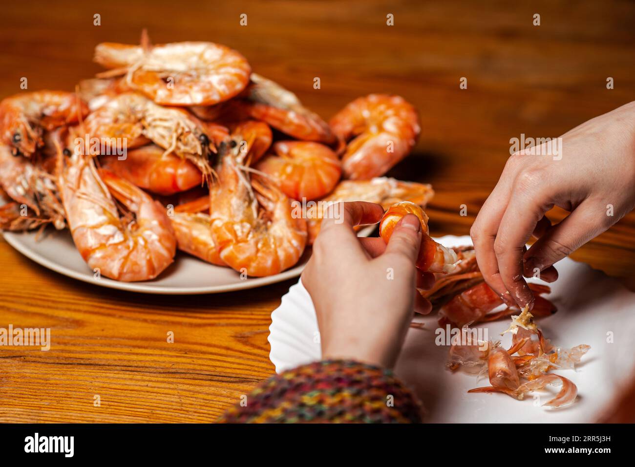 Large cooked king prawns on the table. An unrecognizable man is eating shrimp at the table. Stock Photo