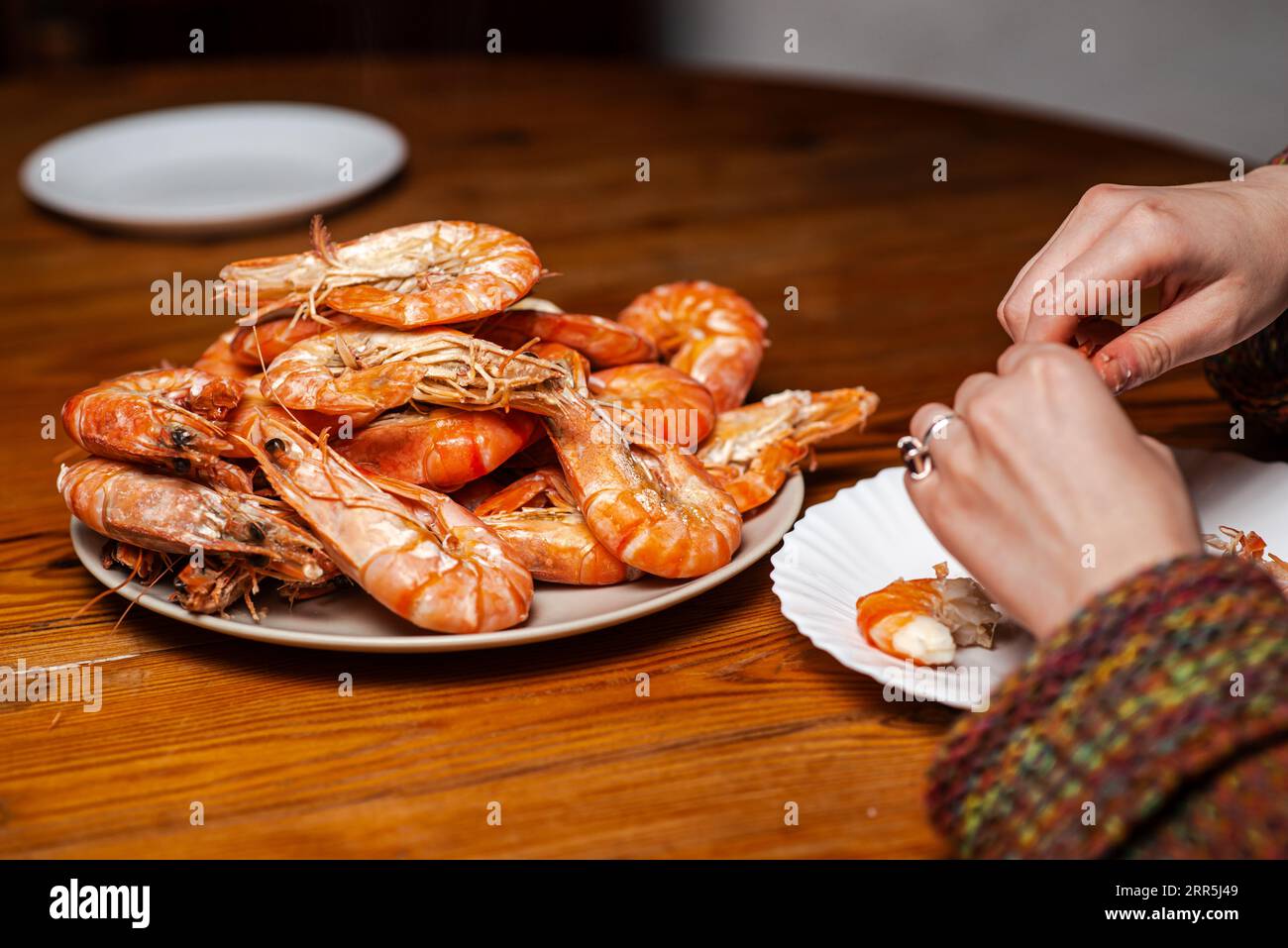 Large cooked king prawns on the table. An unrecognizable man is eating shrimp at the table. Stock Photo