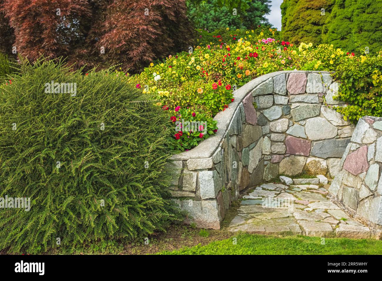 Beautiful garden with grass lawn and flowers in bloom and stone wall ...