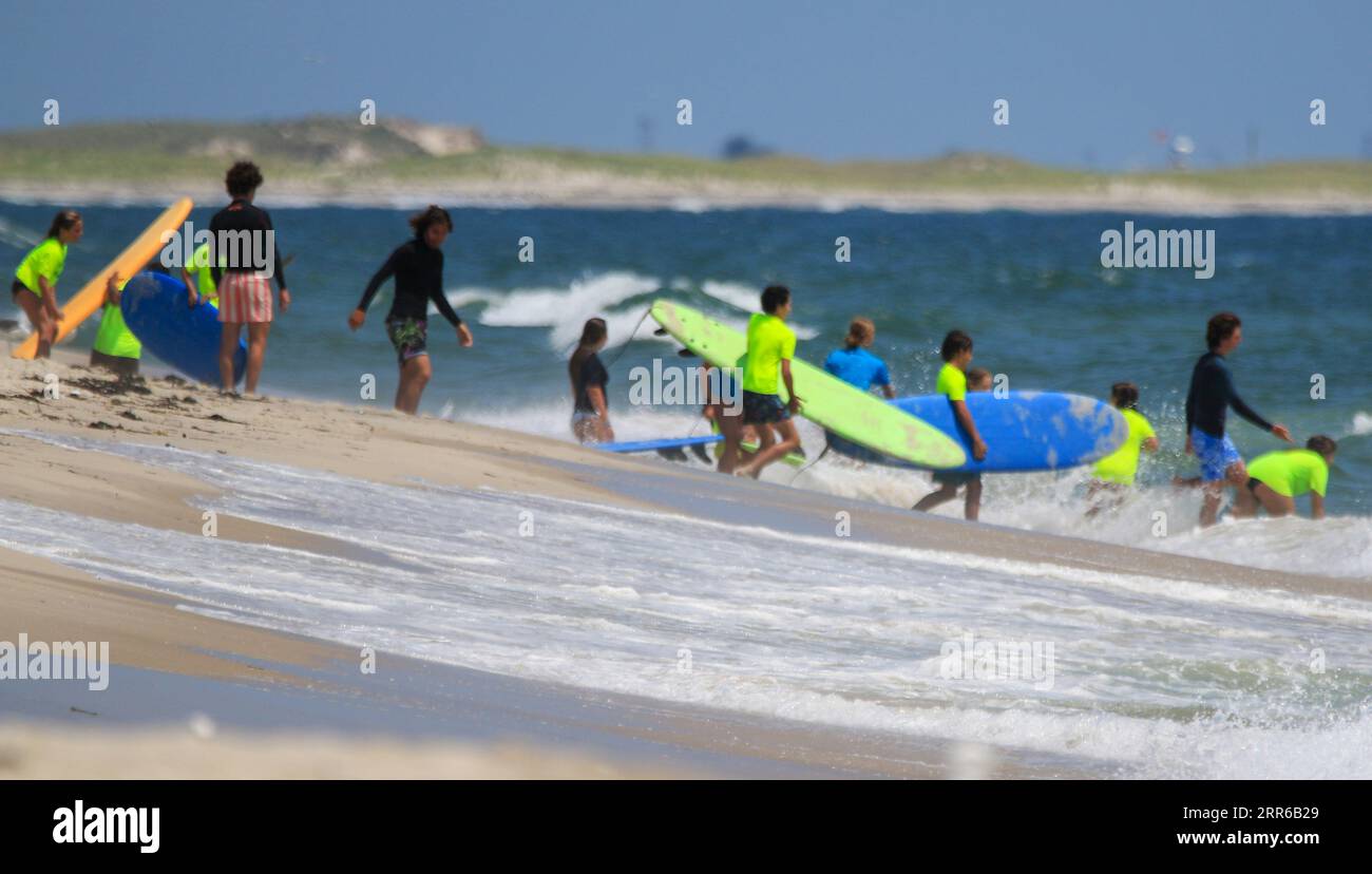 Gilgo Beach, New York, USA - 25 July 2023: Kids in neon green shirts walking into the ocean to go surfing at the Bunger Surf Camp at Gilgo Beach on Lo Stock Photo