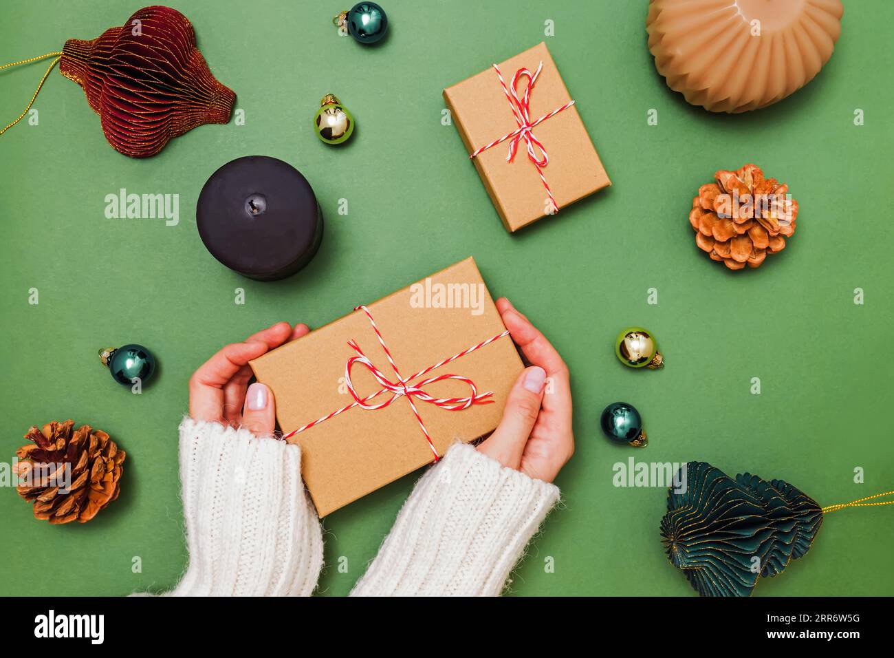Female hands holding gift box, preparing for holidays, Christmas decor on green table, top view Stock Photo