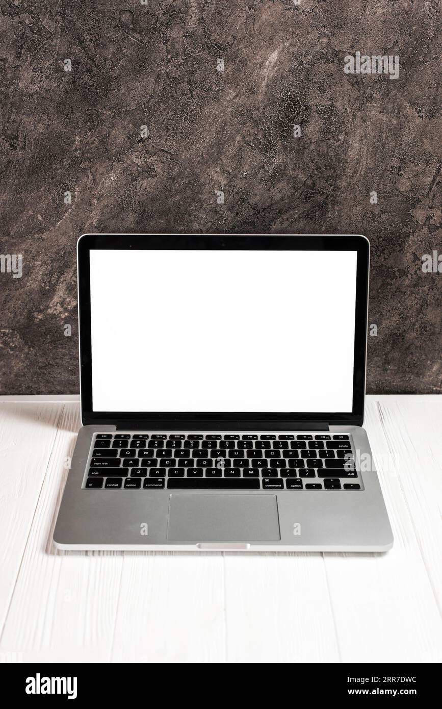 Laptop with blank white screen white wooden table against concrete ...