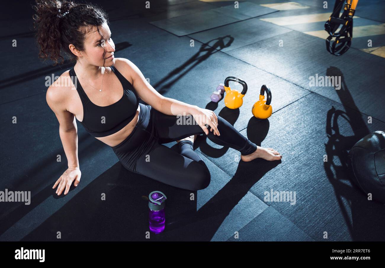 Athletic woman sitting near exercise equipments gym Stock Photo