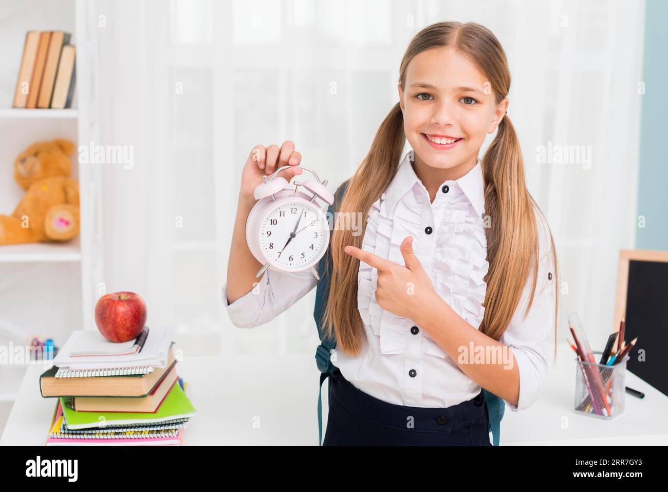 Positive schoolgirl pointing clock Stock Photo