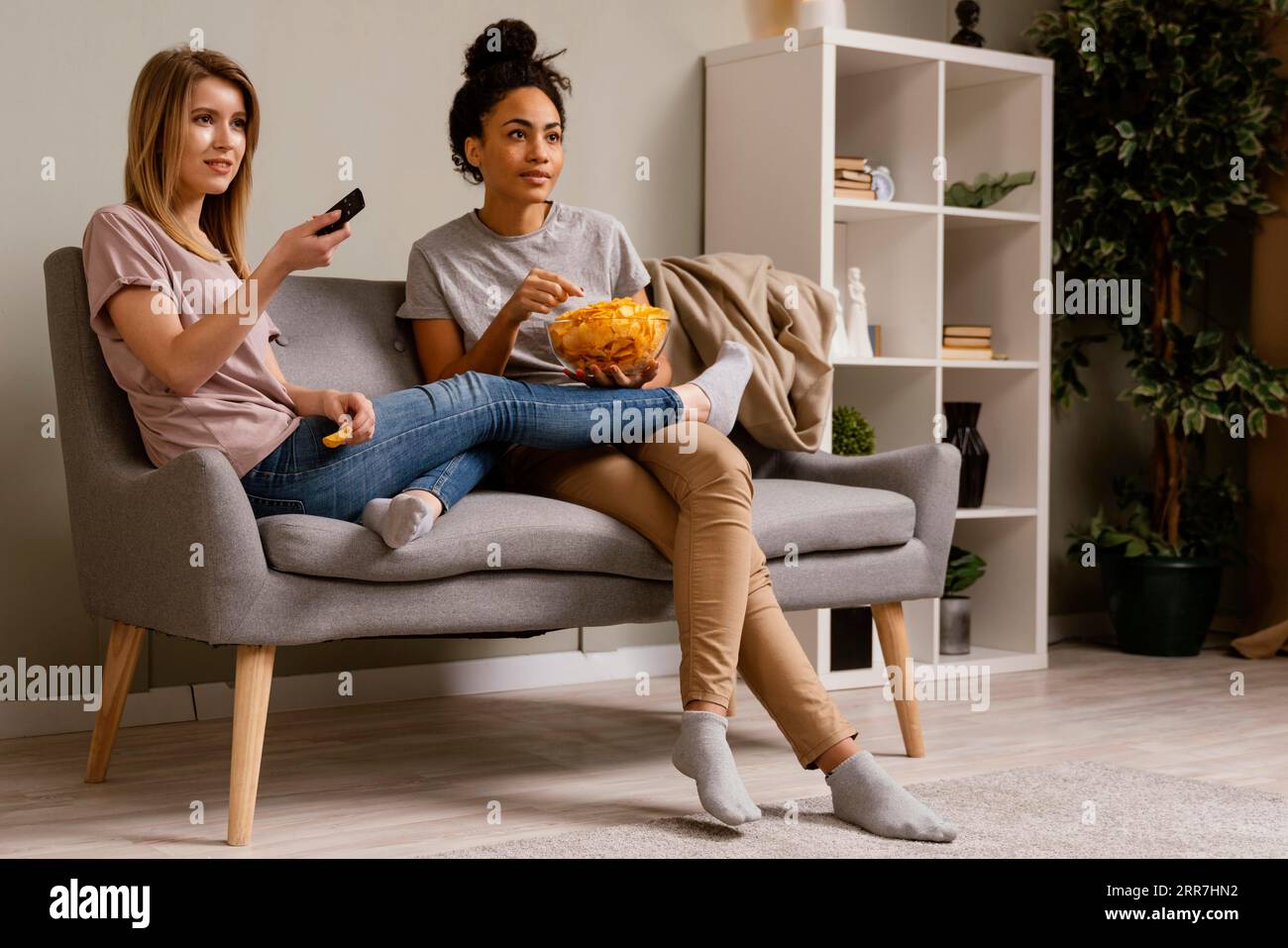 Women couch watching tv eating chips Stock Photo