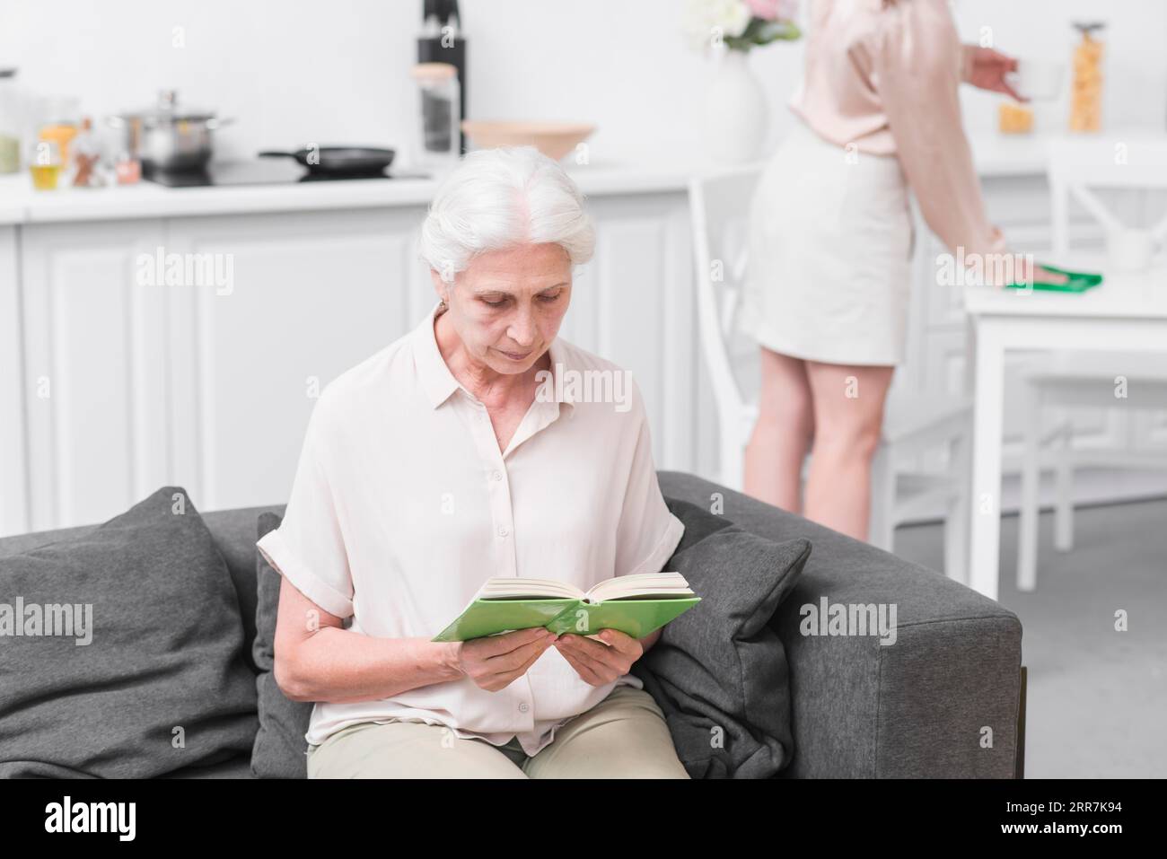 Senior woman sitting sofa reading book home Stock Photo - Alamy