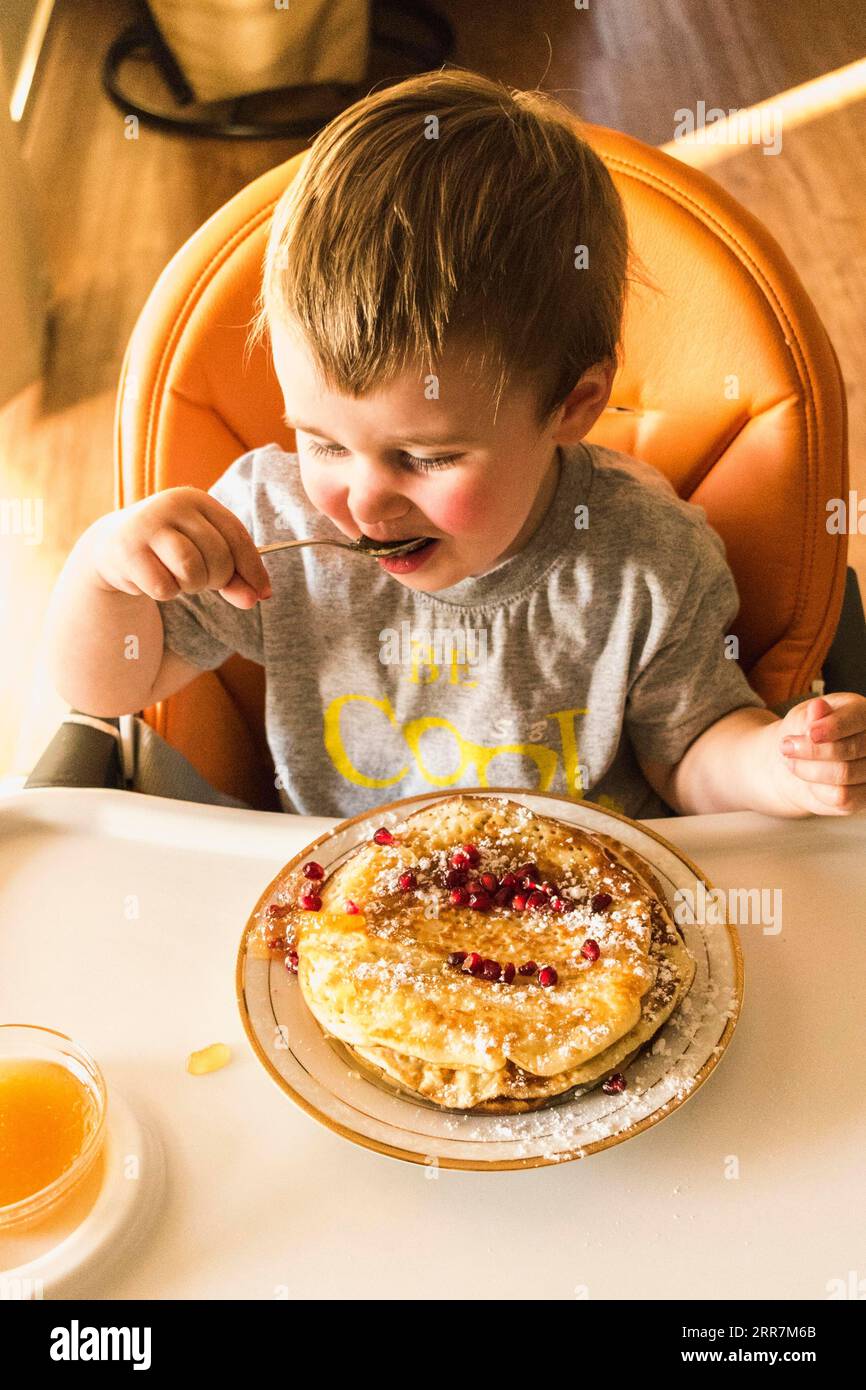 Cute little baby eating pancake plate high chair Stock Photo