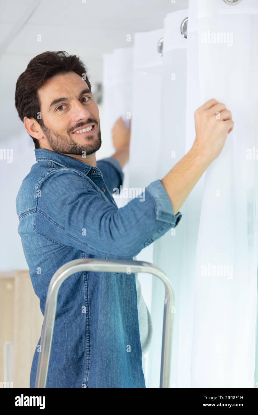 young man installing curtains over window Stock Photo