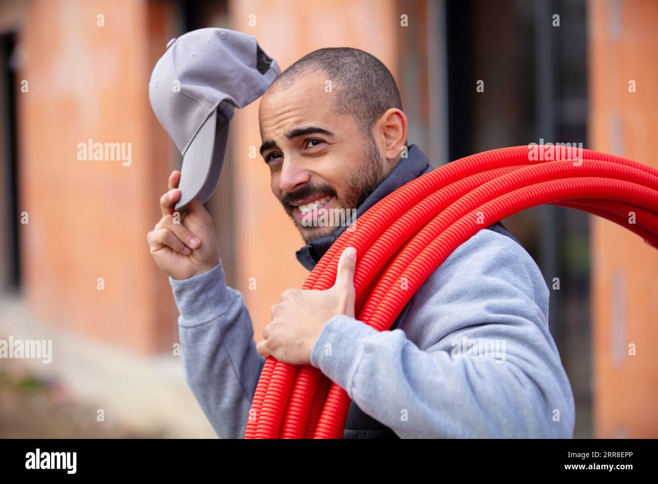workman with roll of red corrugated plastic tubing Stock Photo