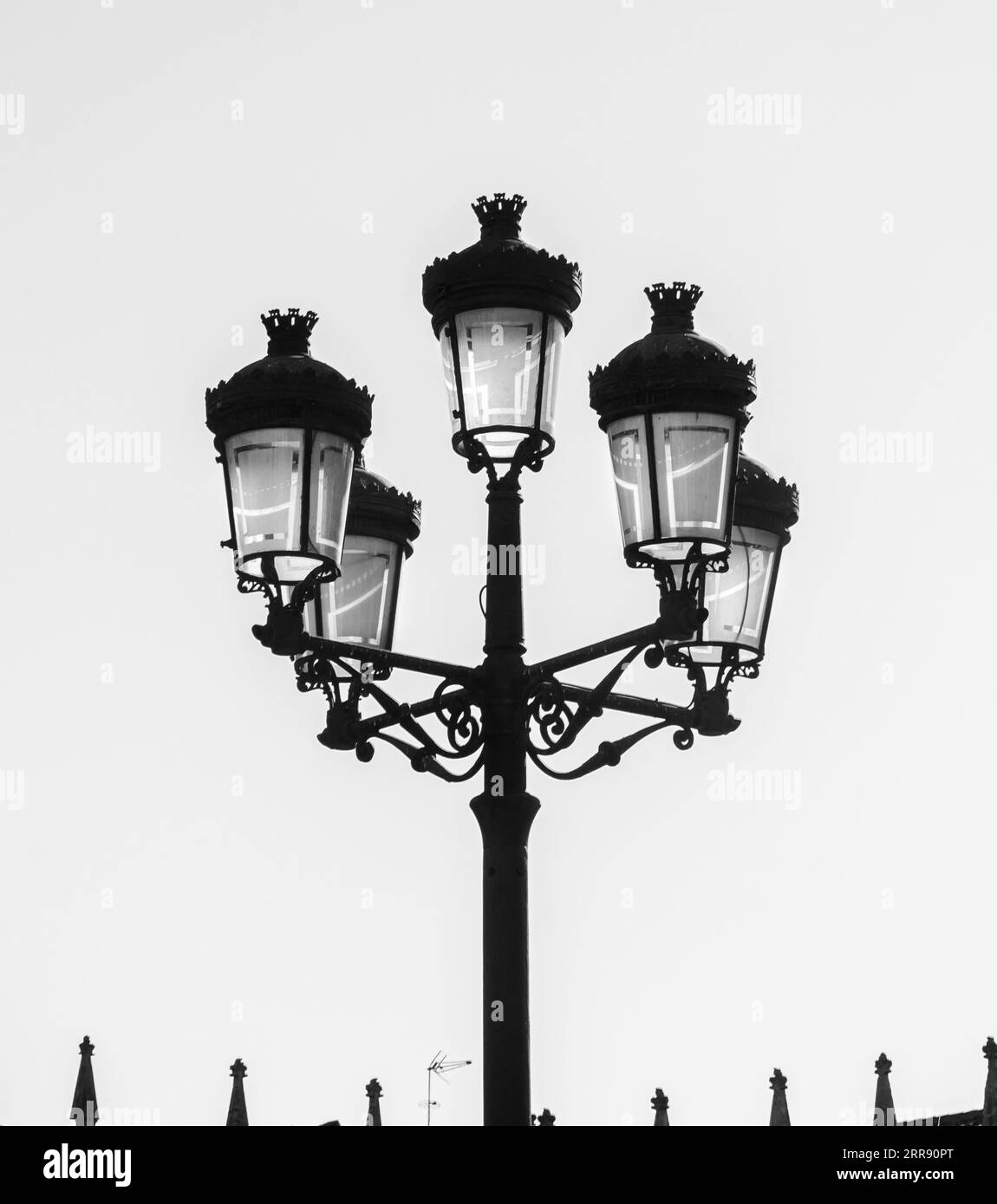 Silhouette of a wrought iron street lamp with five lanterns hand-decorated with opaque glass and a silhouette of a TV antenna and the peaks of the pal Stock Photo