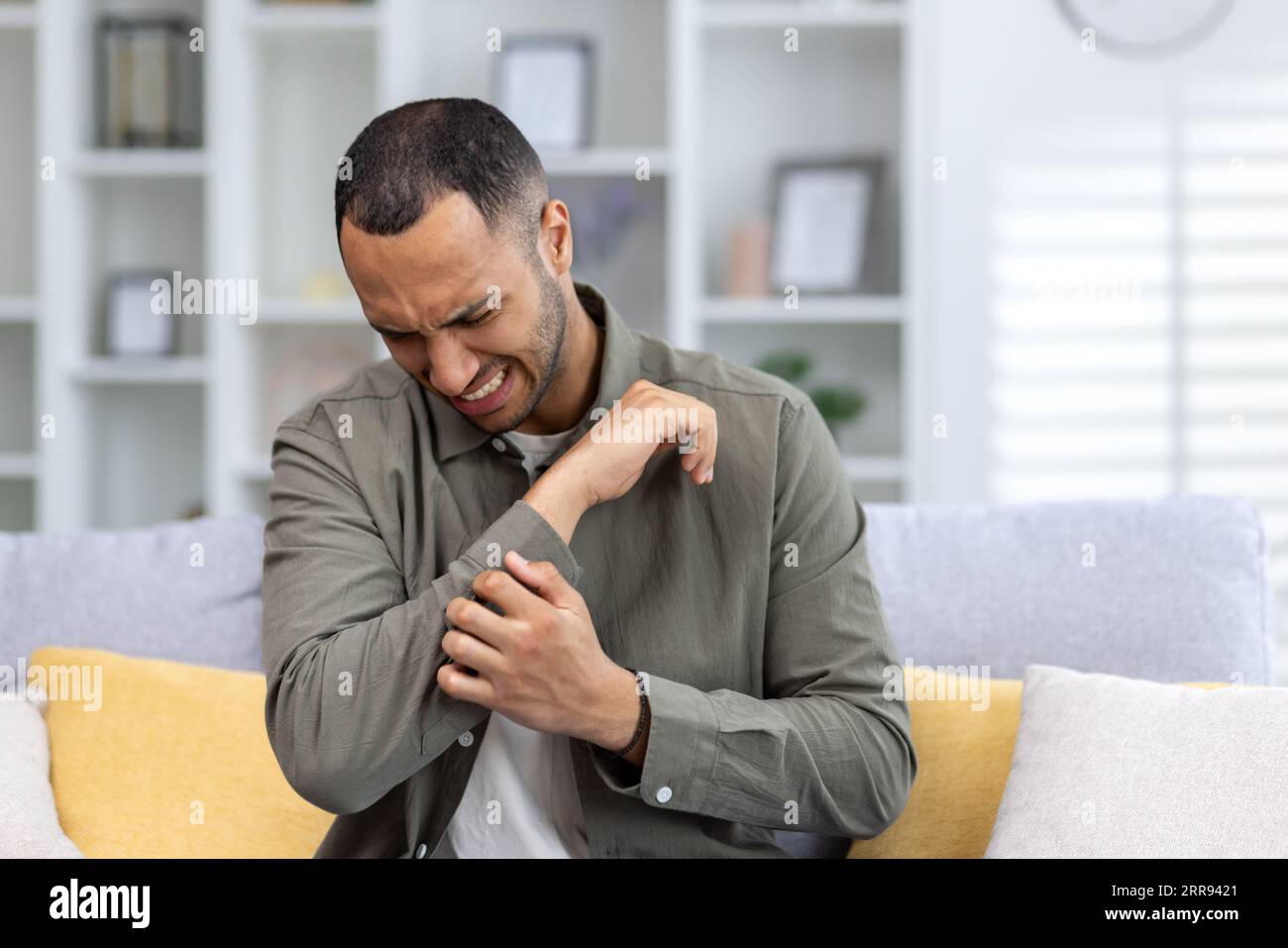 Closeup photo of a young African American man sitting on the couch at home and holding his hand