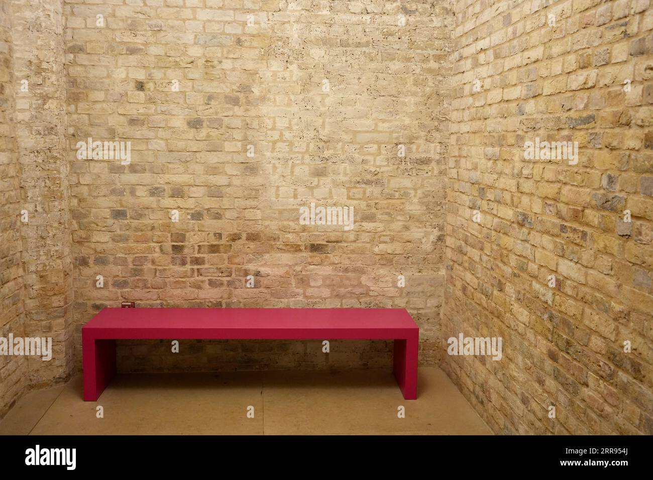 Simple Pink wooden bench in an empty brick room. Stock Photo
