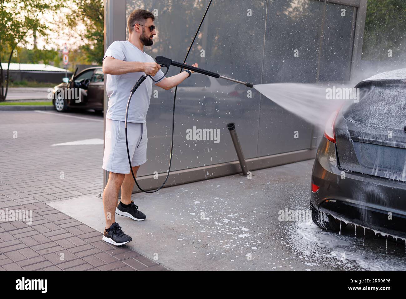 A man washes off foam with a water cannon at a car wash. A car at a self service car wash Stock