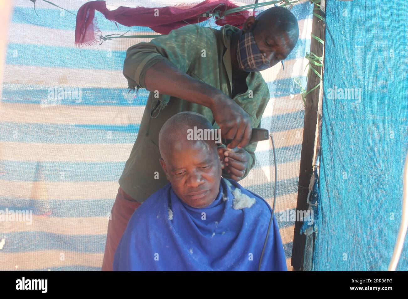 210530 -- FRANCISTOWN BOTSWANA, May 30, 2021 -- Lekang Botlhoko cuts a customer s hair using a device bought from a Chinese shop in Francistown, Botswana, on May 18, 2021. Small and medium businesses in Botswana s capital of Gaborone and second largest city of Francistown have resorted to installing solar panels obtained from nearby Chinese shops dotted across the major cities of the country. Hairdressers and secretarial service providers have designed makeshift saloons powered by solar panels at open spaces in order to continue eking out a living after failing to pay rentals and high electric Stock Photo