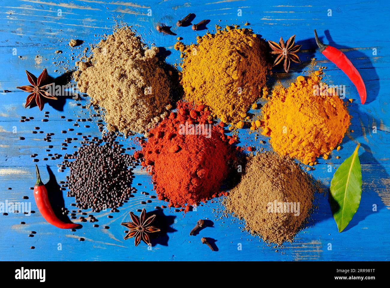 variety of curry powder ingredients on blue painted table top Stock