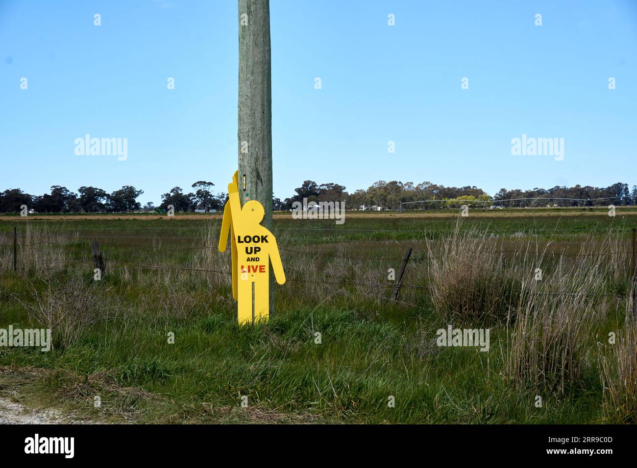 Yellow Human silhouette pointing up reminding of overhead power lines Stock Photo