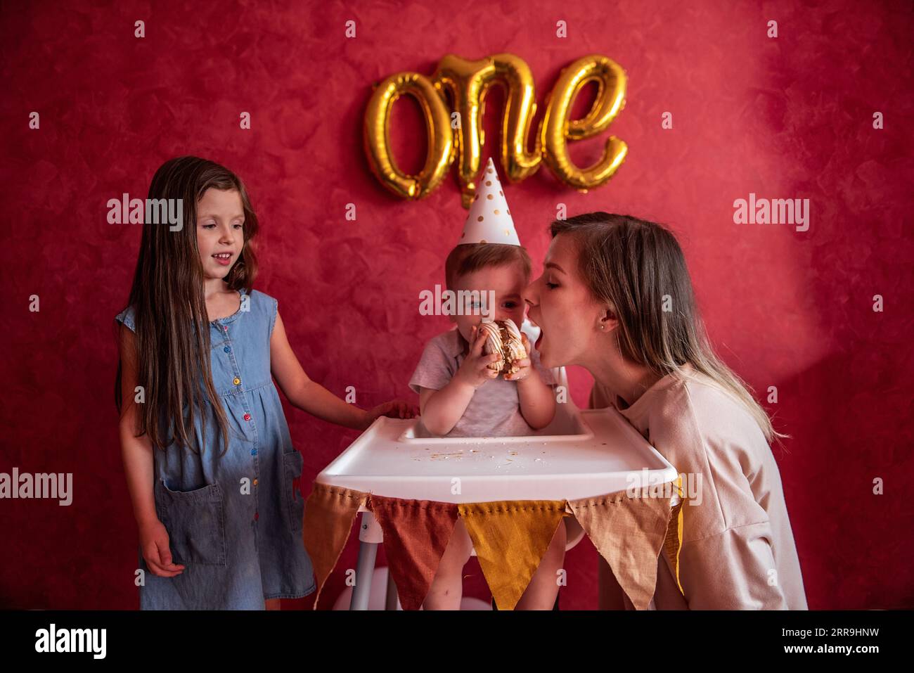 Older sister and mother help little boy blow out candle for his first