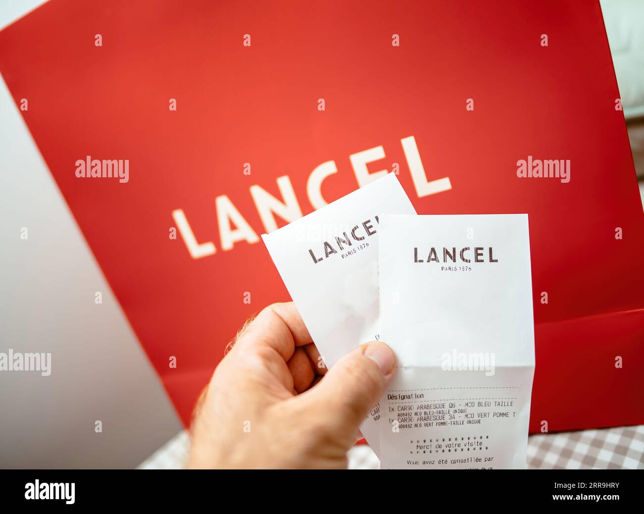 Paris, France - Aug 25, 2023: POV male hand holding Lancel fashion house store receipt with gift bag with logotype in background Stock Photo