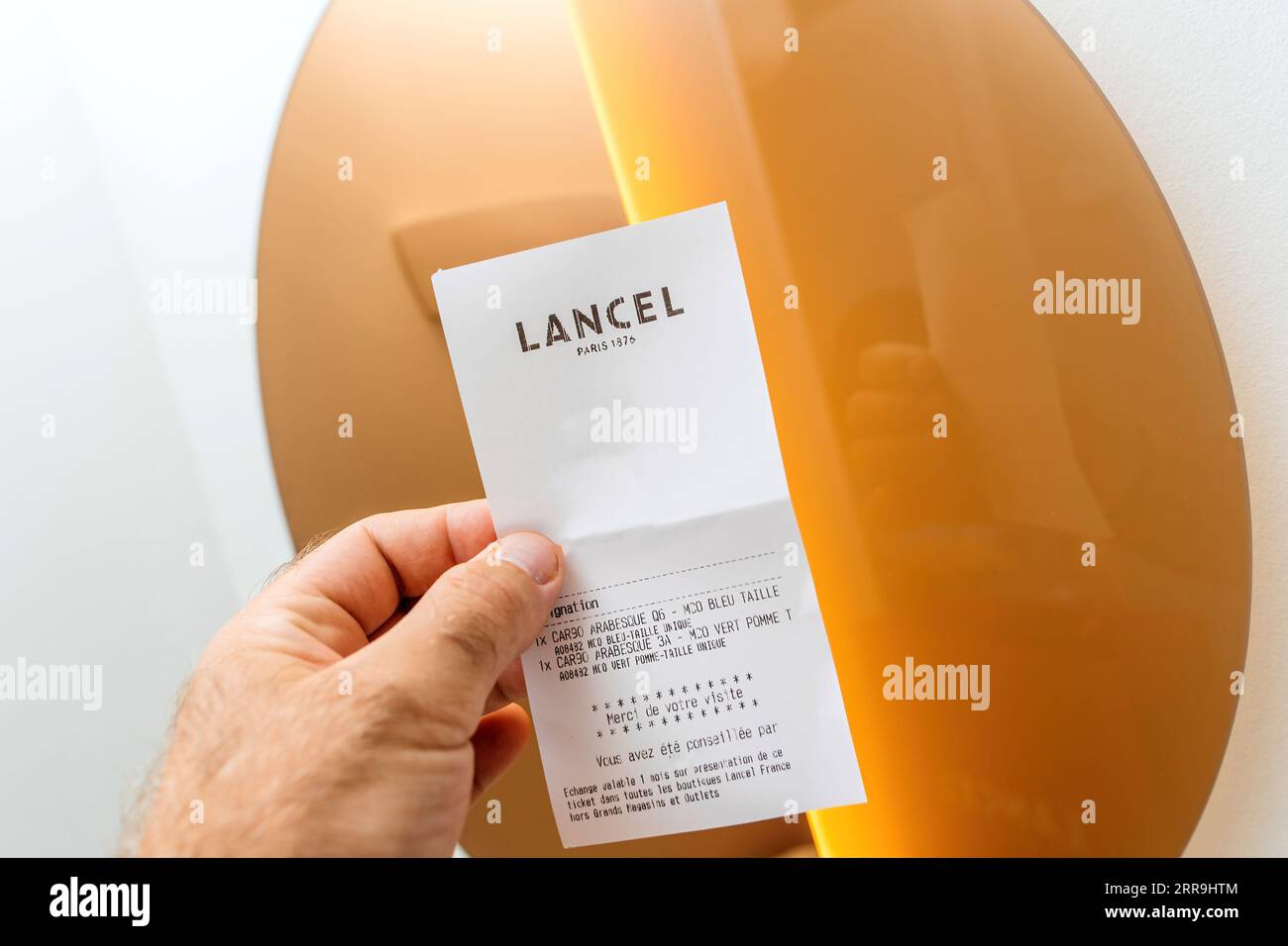 Paris, France - Aug 25, 2023: POV male hand holding Lancel fashion house store receipt against the golden mirror Stock Photo