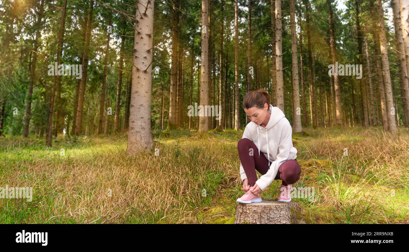Sporty woman tying her running shoes in preperation for running in the forest. Stock Photo