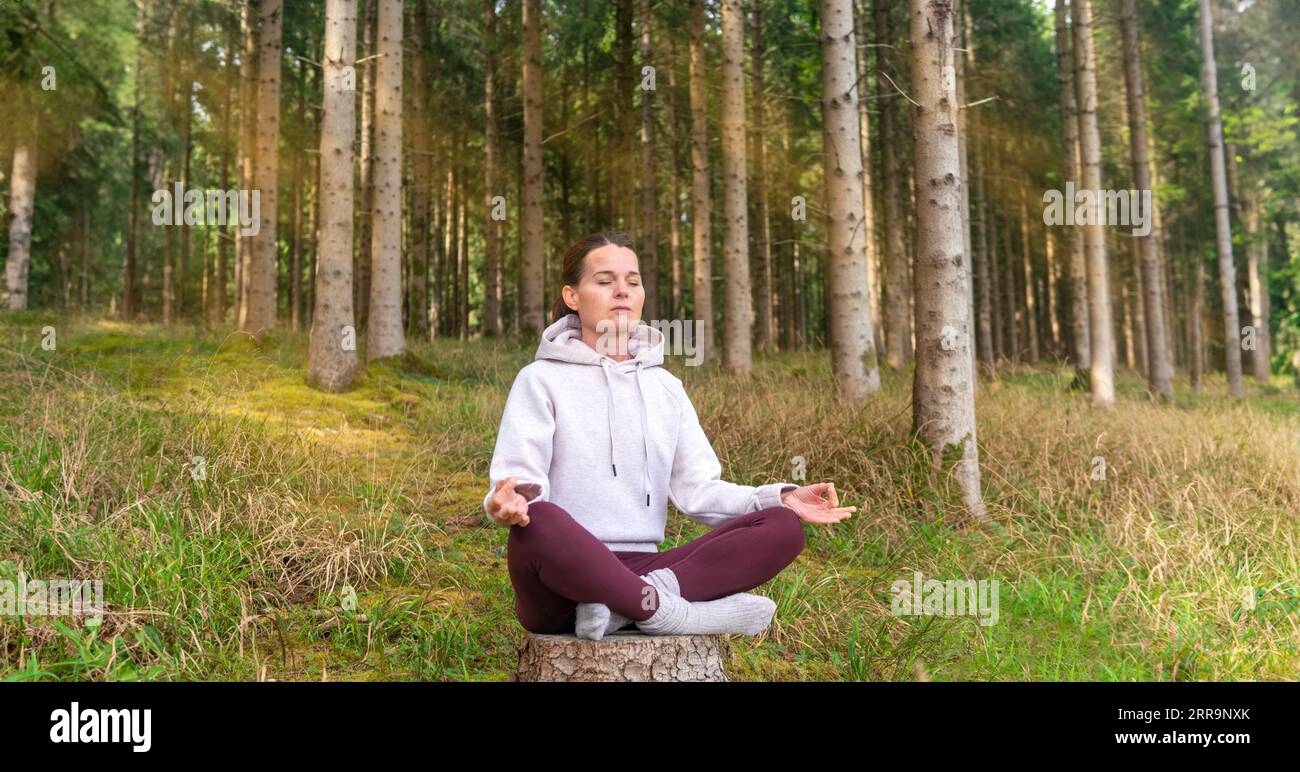 Sporty mid adult woman meditating in a forest. Stock Photo