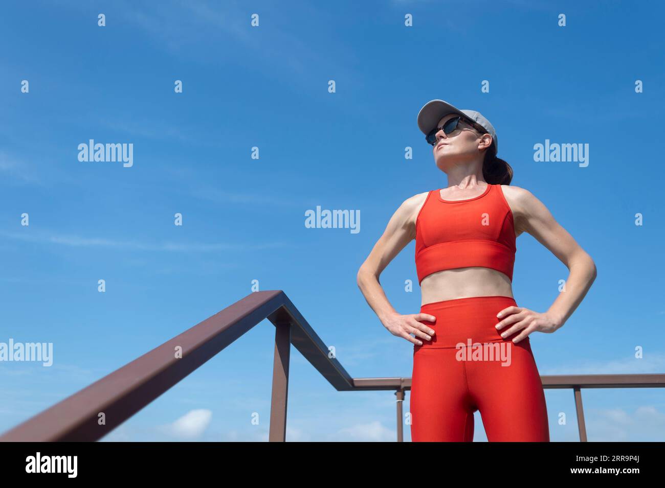 fit, sporty woman standing with hands on her hips looking off. Resting after exercise outside. Stock Photo
