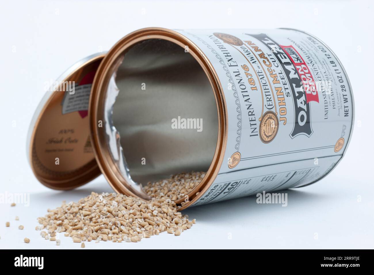 Empty 28 Ounce Can of John McCann Steel Cut Oat Meal Spilling onto a White Surface with Lid Stock Photo