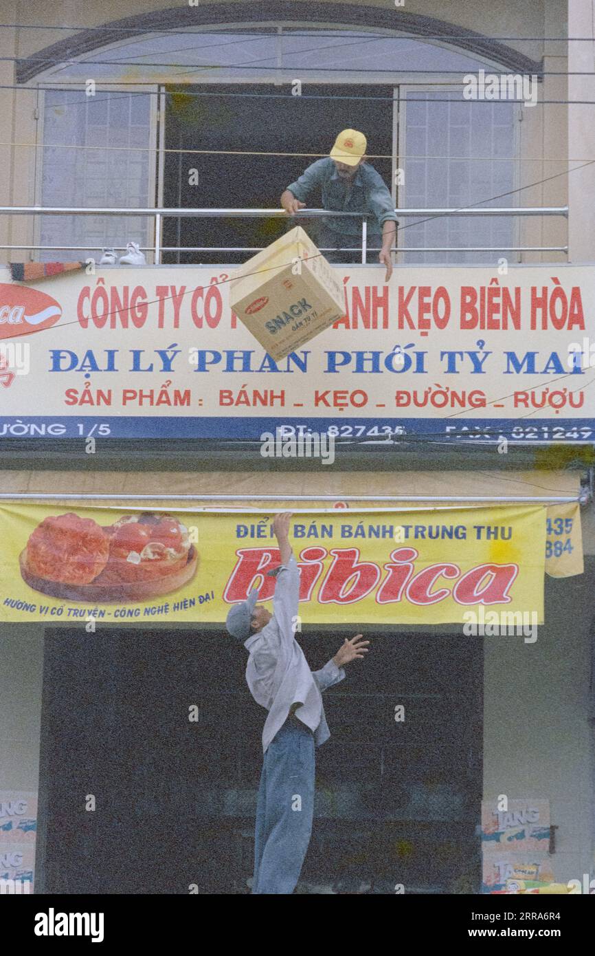 Two local Vietnamese workers throwing up boxes into storage at their shophouse in Saigon Stock
