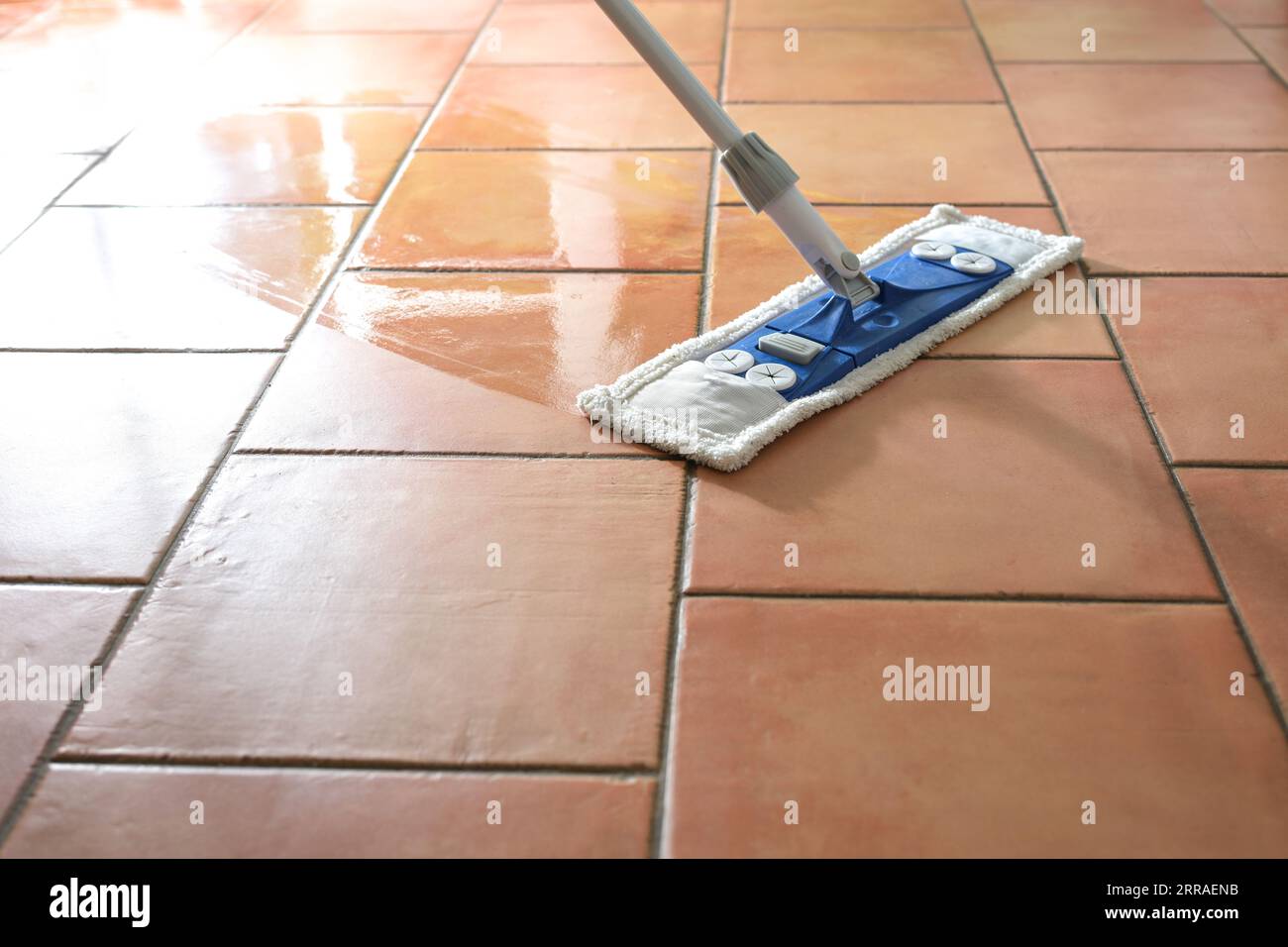 Flat wet-mop made of microfiber wipes the tiled terracotta floor, daily cleaning routine for a hygienic and healthy home, copy space, selected focus, Stock Photo