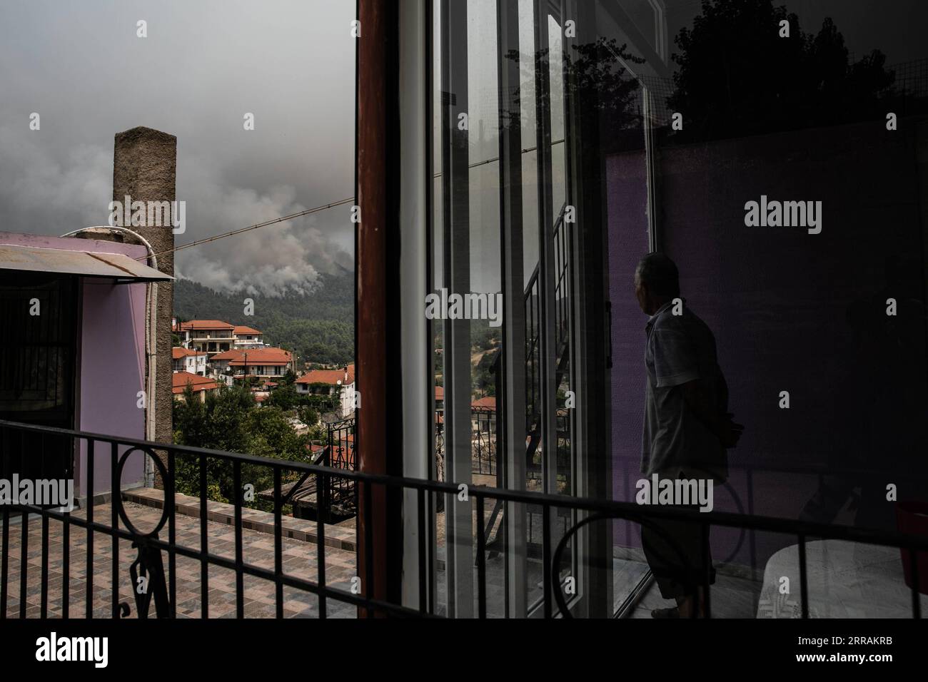 210806 -- EVIA, Aug. 6, 2021 -- A man watches clouding smog from a wildfire at his house in the north of Evia island, Greece, on Aug. 5, 2021. Greek Prime Minister Kyriakos Mitsotakis said on Thursday evening that Greece is facing an extremely critical situation with multiple forest fires at the same time, while saving human lives is the government s top priority. Wildfires in the north of Athens leapt back to life on Thursday as Greece also faces flare-ups on the island of Evia, in Ancient Olympia in the northwestern Peloponnese and in other parts of the country. TO GO WITH Greek PM says savi Stock Photo
