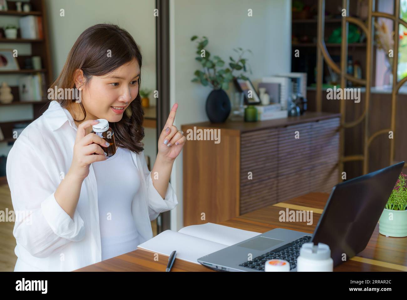 From home's comfort, an Asian pregnant woman consults her doctor through the digital realm. A pill bottle holds hope as virtual care bridges distances Stock Photo