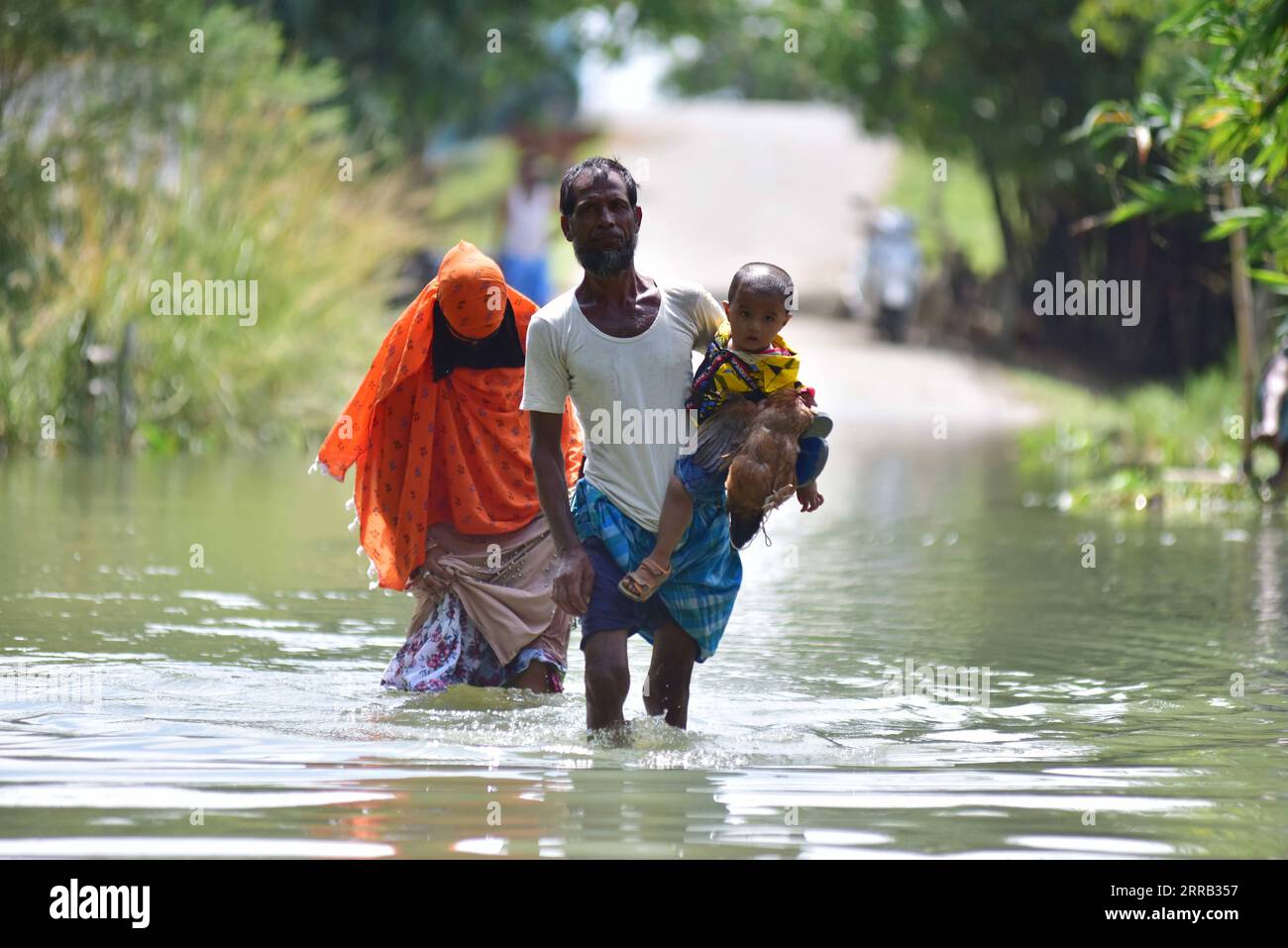 210829 -- MORIGAON, Aug. 29, 2021 -- A man carries his child as his family wades through a waterlogged road in a village in Morigaon district of India s northeastern state of Assam, Aug. 28, 2021. Str/Xinhua INDIA-ASSAM-MORIGAON-FLOOD JavedxDar PUBLICATIONxNOTxINxCHN Stock Photo