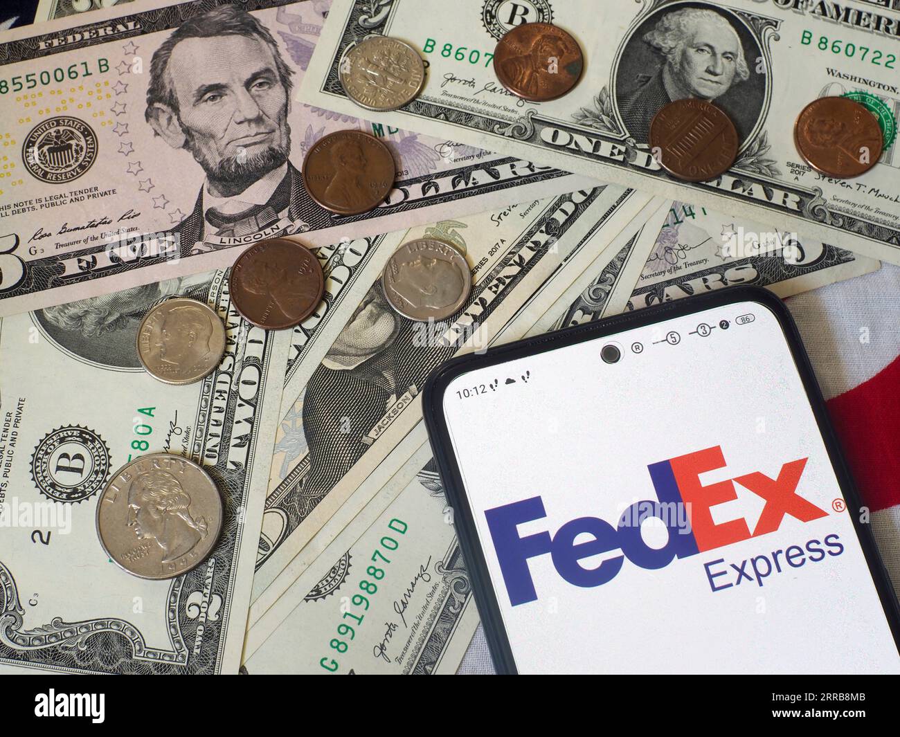 In this photo illustration, the FedEx Corporation logo is seen displayed on a smartphone and US currency notes and coins in the background. Stock Photo