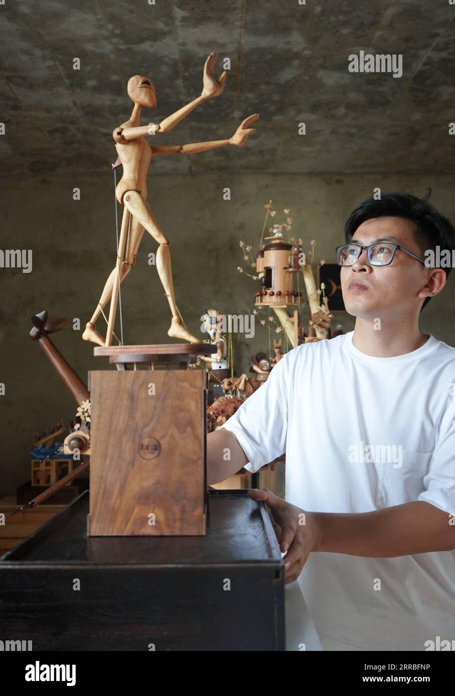 210919 -- SHIJIAZHUANG, Sept. 19, 2021 -- Li Zhanlong shows a wooden mechanical installation at his studio in Luquan District of Shijiazhuang, north China s Hebei Province, Sept. 14, 2021. Li Zhanlong is a wooden mechanical installation designer in Shijiazhuang. After graduation, Li once worked as a salesman and ran an online shop. In 2018, Li Zhanlong left his job and went to Tianjin to learn carpentry skills. The wooden mechanical installation consists of a wooden figure and a mechanism device that can make the installation move. By shaking the handle or pressing the button, the installation Stock Photo