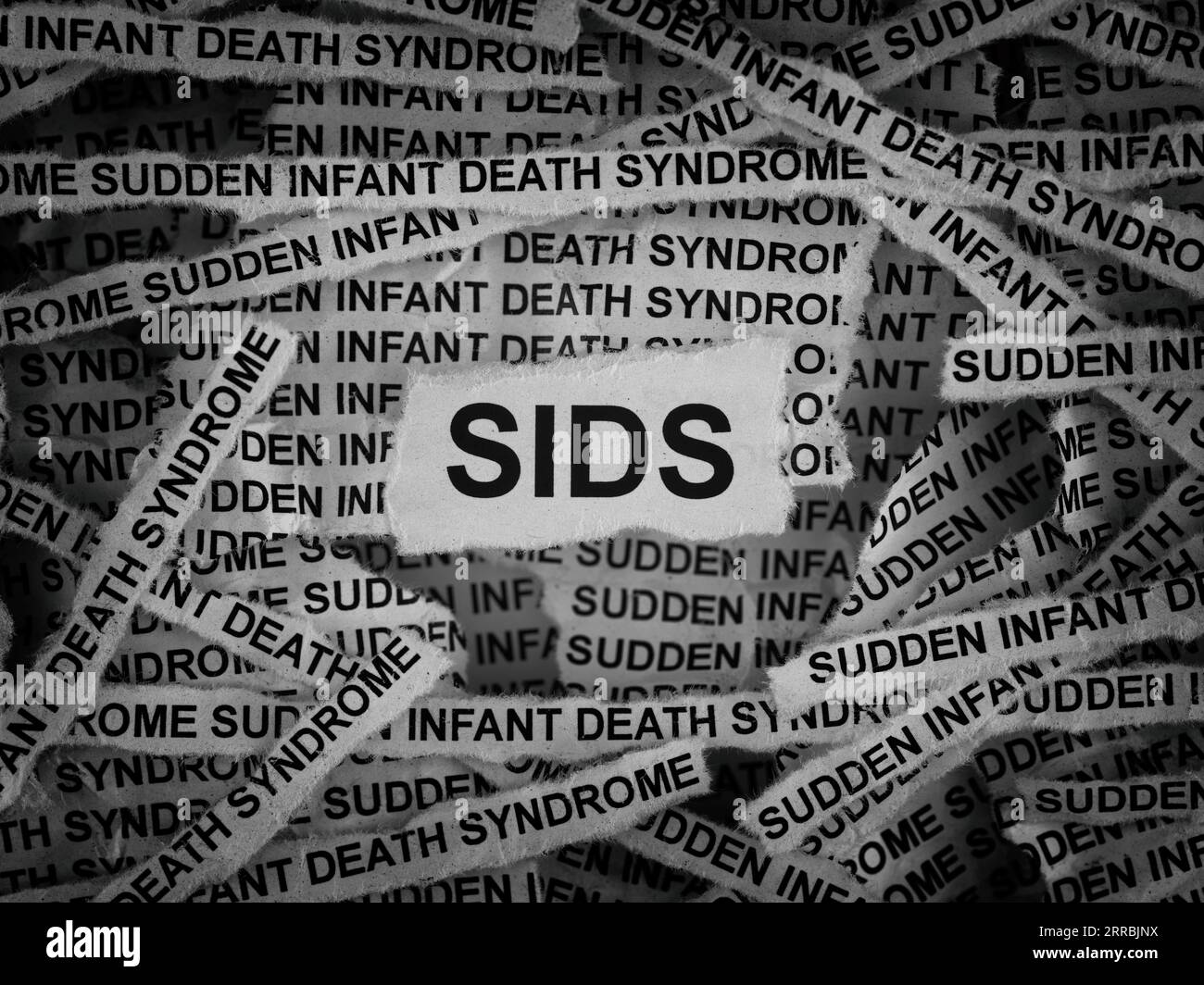 Strips of newspaper with the words SIDS (Sudden Infant Death Syndrome) typed on them. Black and white. Close up. Stock Photo