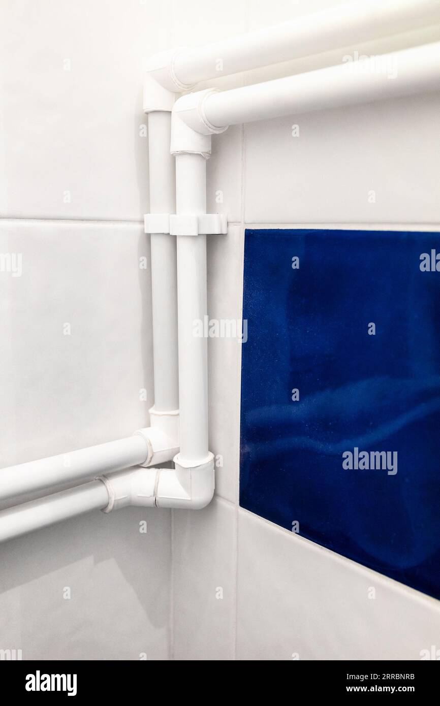 new connected white polypropylene pipes in corner of bathroom on wall covered with ceramic tiles Stock Photo