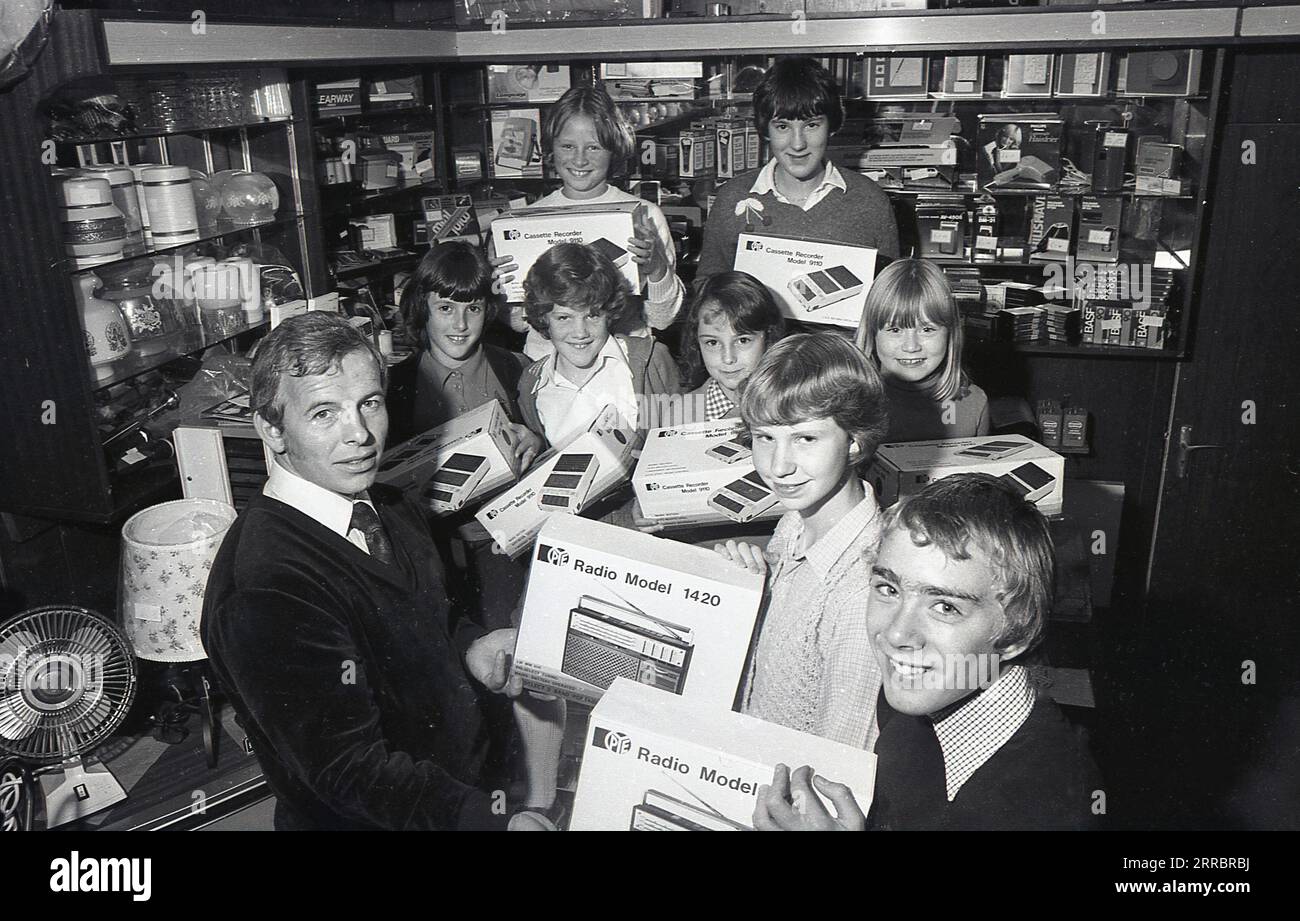 1981, inside a home appliances or electrical shop, a male shopkeeper  with excited young school children with their prizes of the latest portable transistor radios and cassette recorders, England. UK. The young wnners are holding  the Pye Radio Model 1420, while the cassette recorder is a Pye Model 9110. The Pye brand dates back to 1896 when William Pye started making scientific instruments in Cambridge under the name W. G Pye Ltd and then 1922 wireless components. In 1928 Pye sold the business, now called Pye Radio Ltd to C.O Stanley. Stock Photo