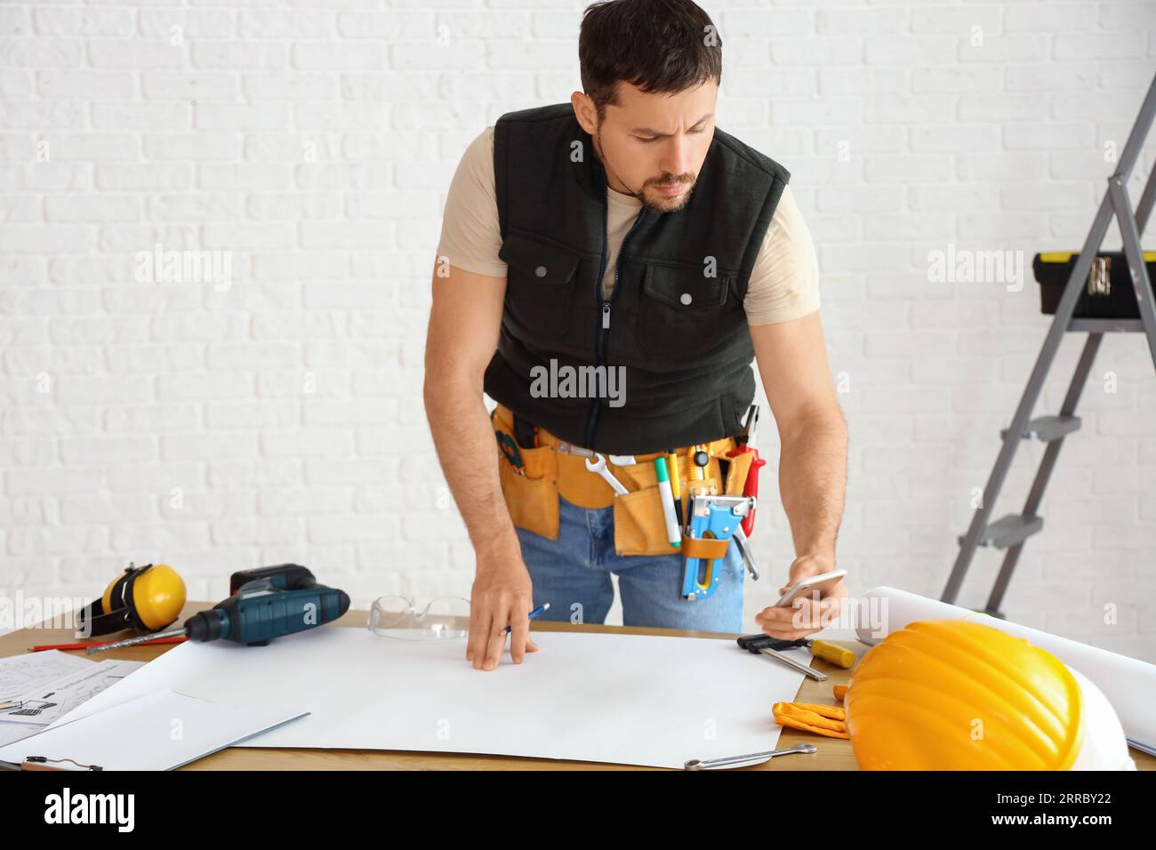 Male builder working with house plan at table in room Stock Photo - Alamy