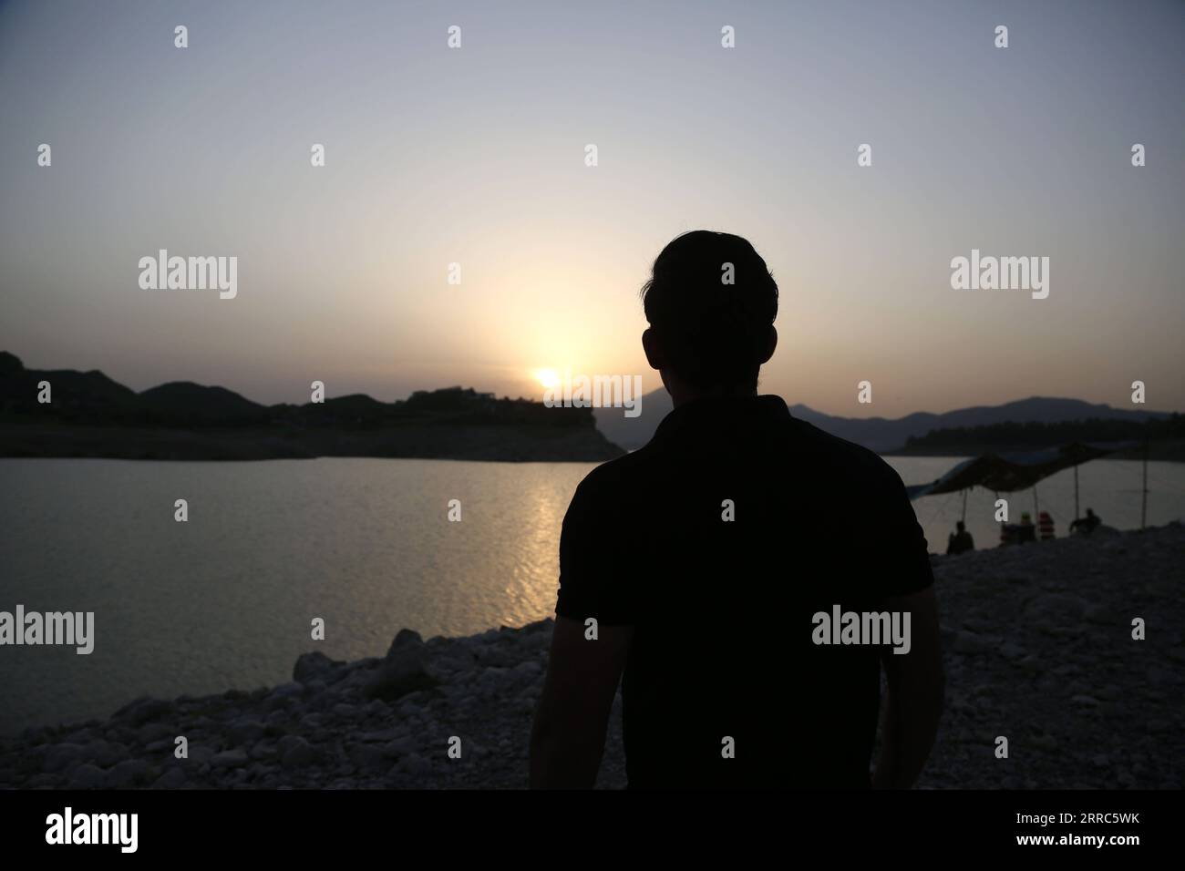 211019 -- KHANPUR, Oct. 19, 2021 -- Photo taken on Oct. 19, 2021 shows a man enjoying the view of sunset at Khanpur Lake in Khanpur of Pakistan s northwestern Khyber Pakhtunkhwa province.  PAKISTAN-KHANPUR-LAKE-SUNSET AhmadxKamal PUBLICATIONxNOTxINxCHN Stock Photo