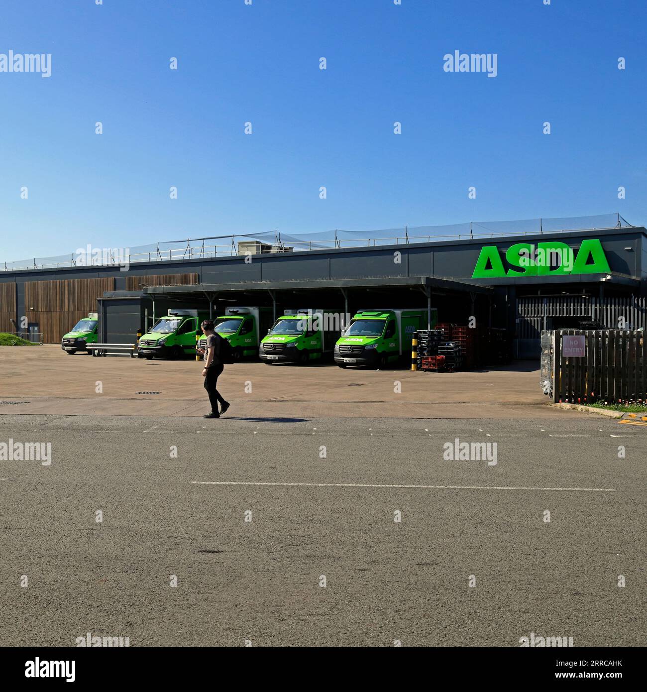 Man walks across entrance to ASDA delivery vans parking area, Barry, South Wales Sept 2023 Stock Photo