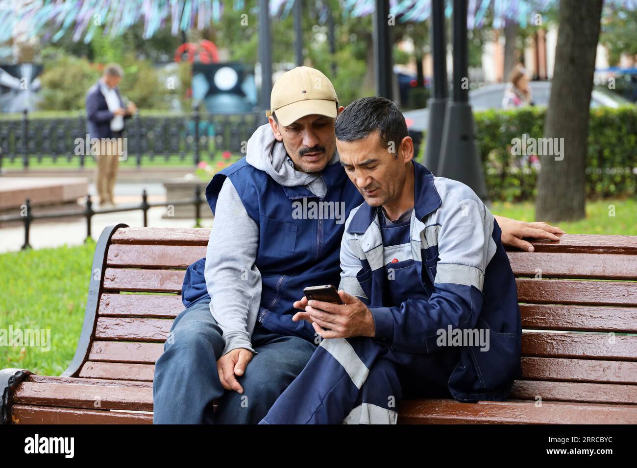 Public utilities workers sitting with smartphone on a bench in autumn city Stock Photo