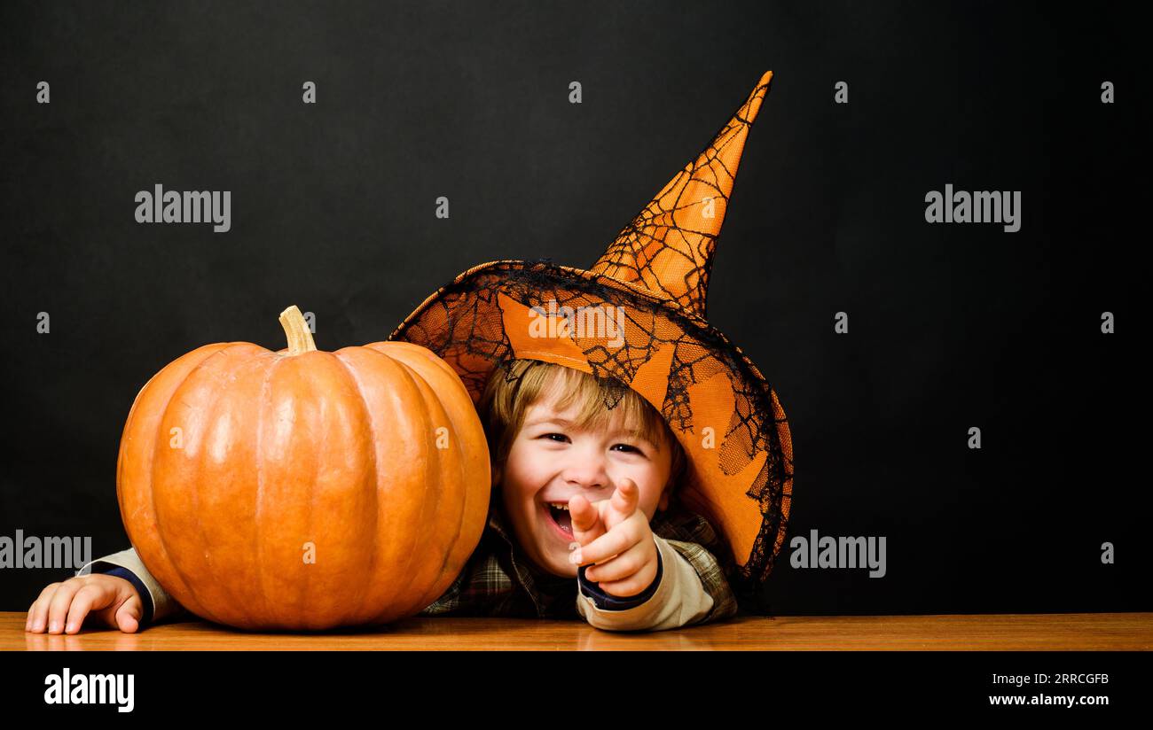 Smiling child boy in witch hat with pumpkin. Halloween holidays. Cute kid with Halloween pumpkin. Autumn recipes. Thanksgiving day cooking. Halloween Stock Photo