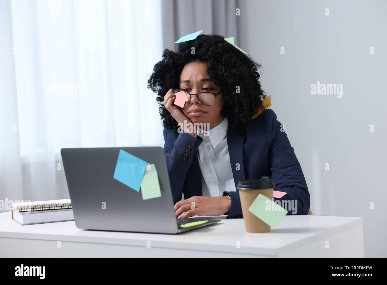 Deadline concept. Tired woman working with laptop in office. Many sticky notes everywhere as reminders Stock Photo