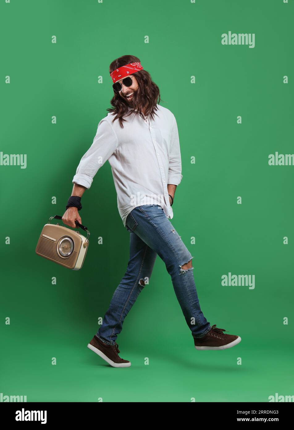 Stylish hippie man in sunglasses with retro radio receiver walking on green background Stock Photo