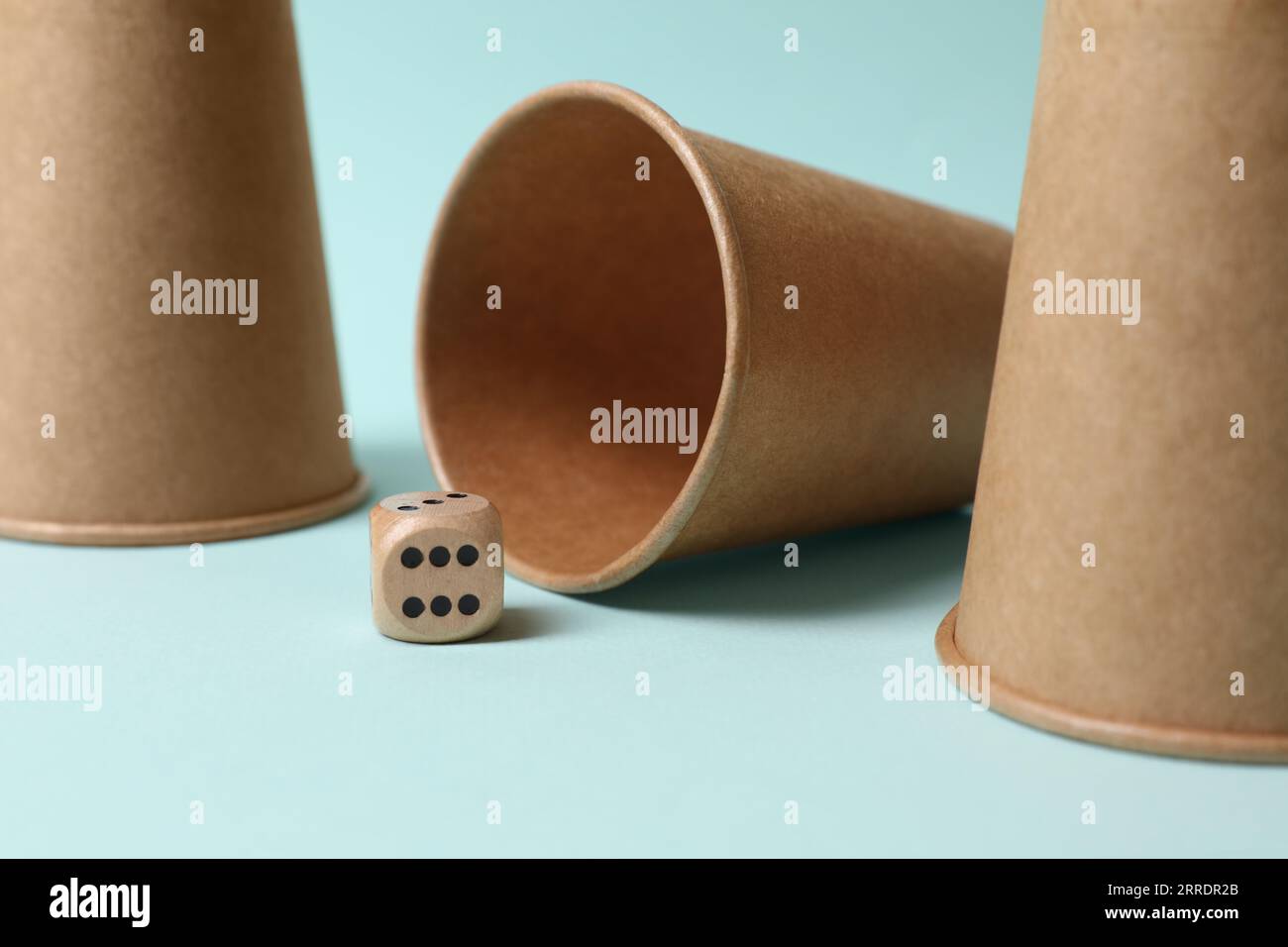 Three paper cups and dice on light blue background, closeup. Thimblerig ...