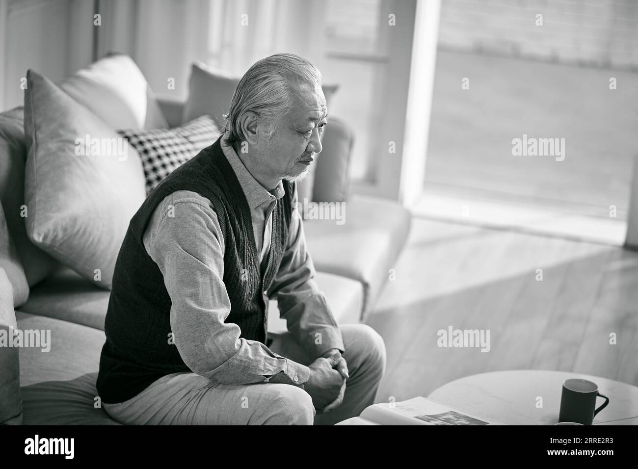 sad asian senior man sitting on couch in living room at home, black and white Stock Photo