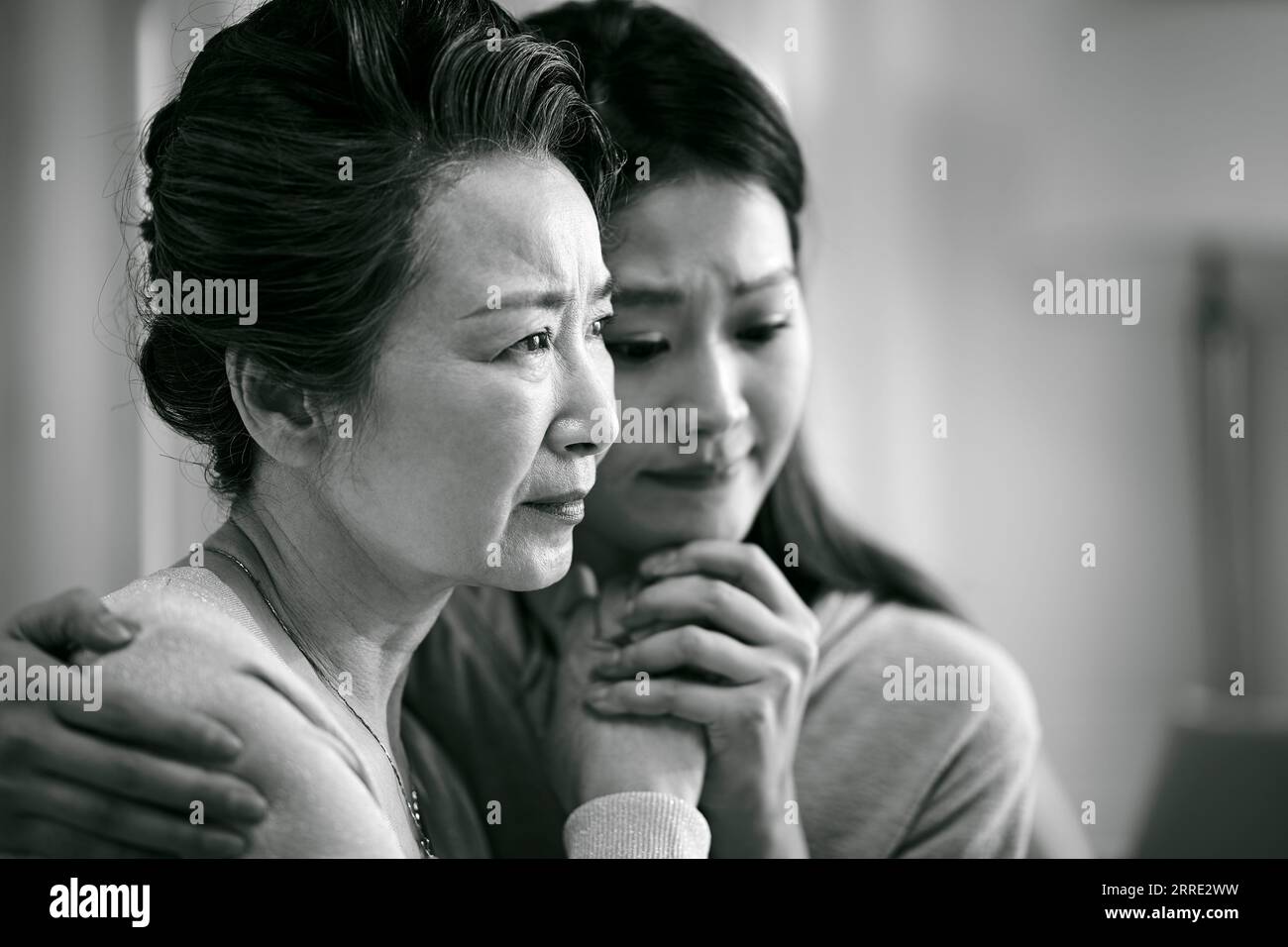 grieving senior asian mother and adult daughter holding hands, black and white Stock Photo